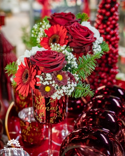 Bouquet de Noël avec roses rouges et gerberas dans un vase décoratif rouge.